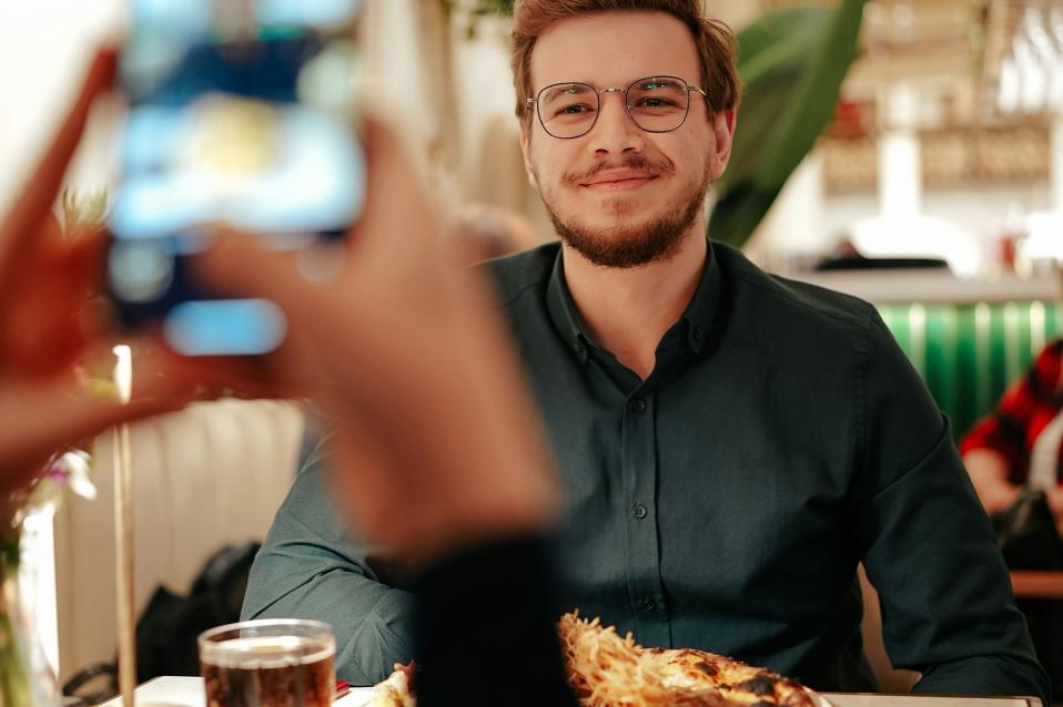 Mann sitzt am Tisch vor Essen und eine Frau mach ein Bild von ihm