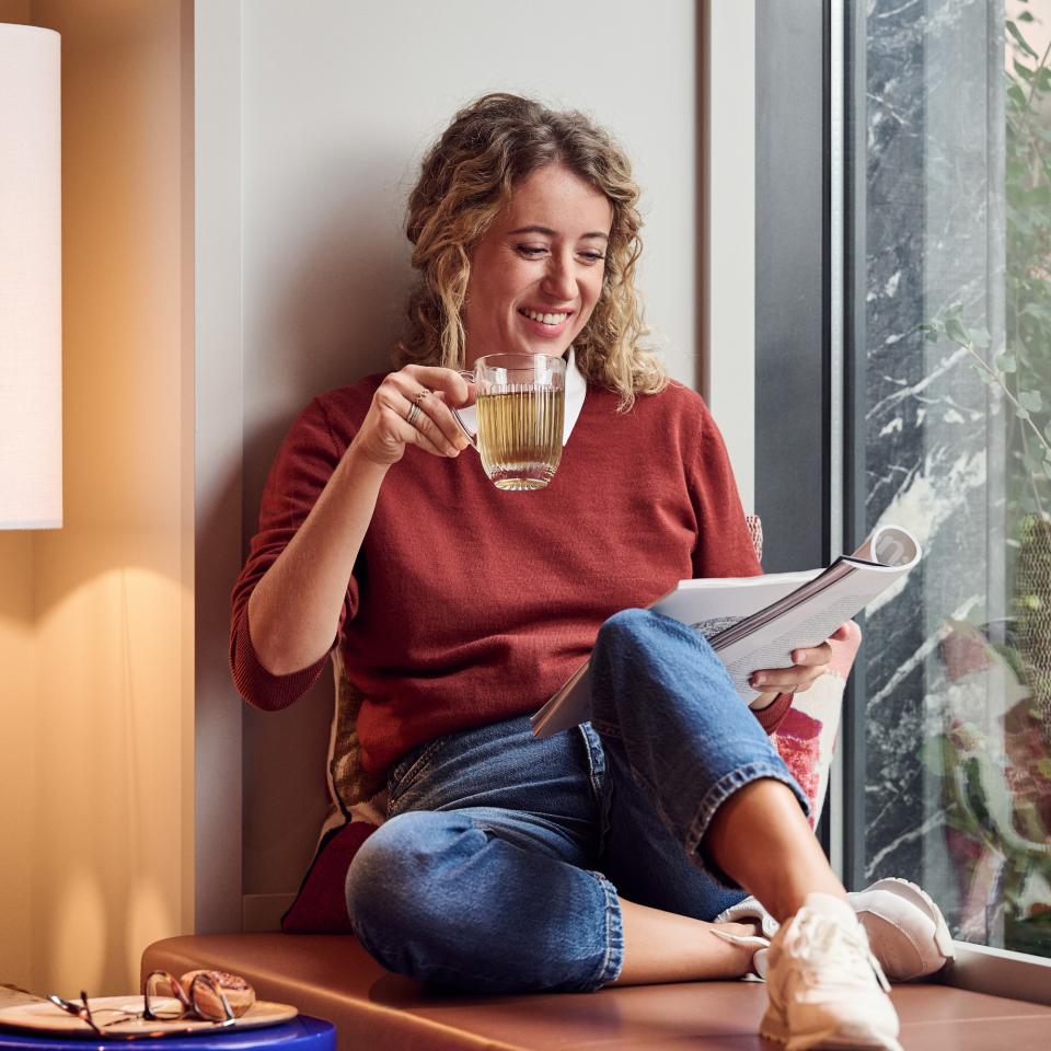 Frau sitzt am Fenster und trinkt Tee