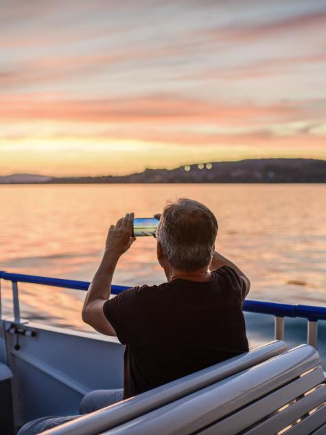 Mann sitz im Schiff auf dem Zürichsee bei Abendstimmung und macht ein Bild