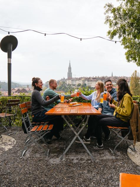 Gruppe von Freunden stösst gemeinsam an und sitzt auf der Terrasse des Tramdepots